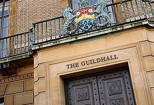 The front of The Guildhall in Cambridge. The crest is central on the metal balustrade on the balcony above the ornate black double doors